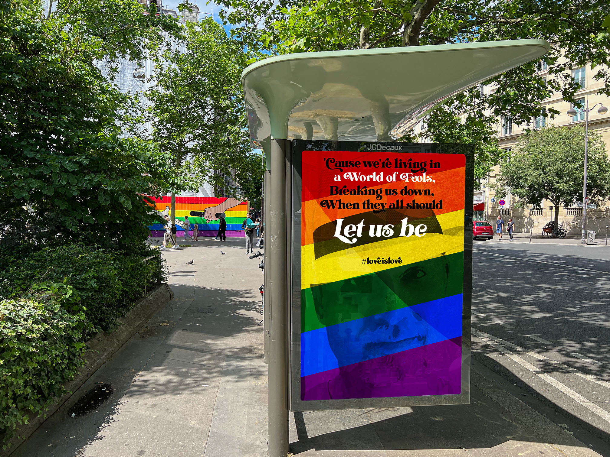 Pride colored poster at a bus stop in Paris with the text "Cause we're living in a world of fools, breaking us down, when they all should let us be. #LoveIsLove"