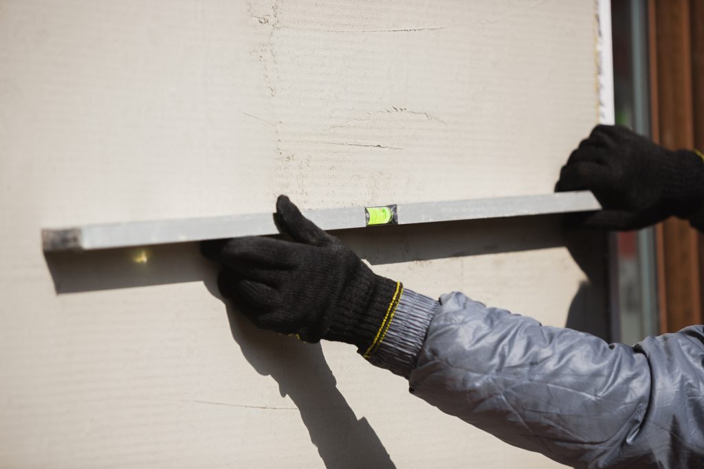 Closeup of repairman in uniform, professional builder working using construction equipment. Process of building, apartment renovation, repairing, building. Coloring, measuring, preparing the base.