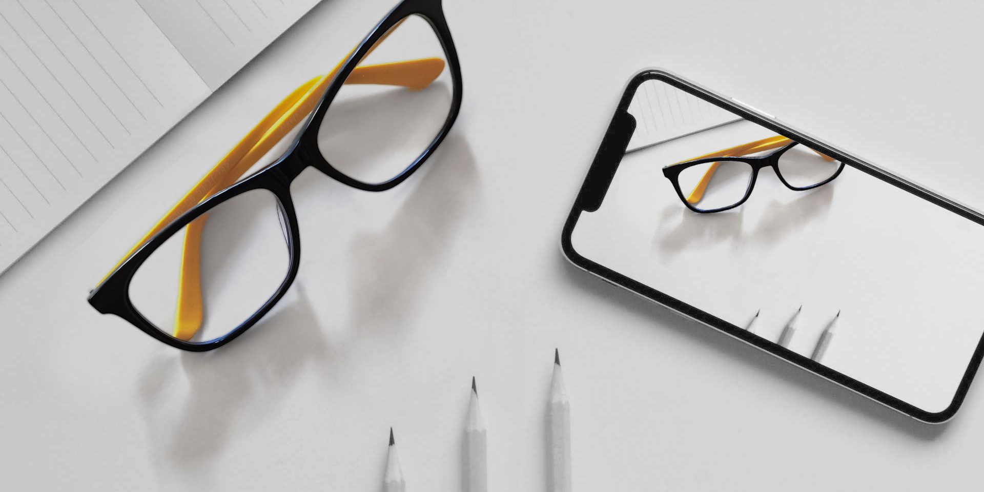 Schreibtisch mit Bleistifen, Brille und Smartphone
