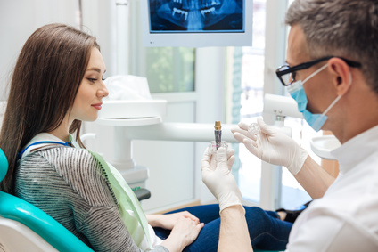 Male dentist showing his female patient a dental implant