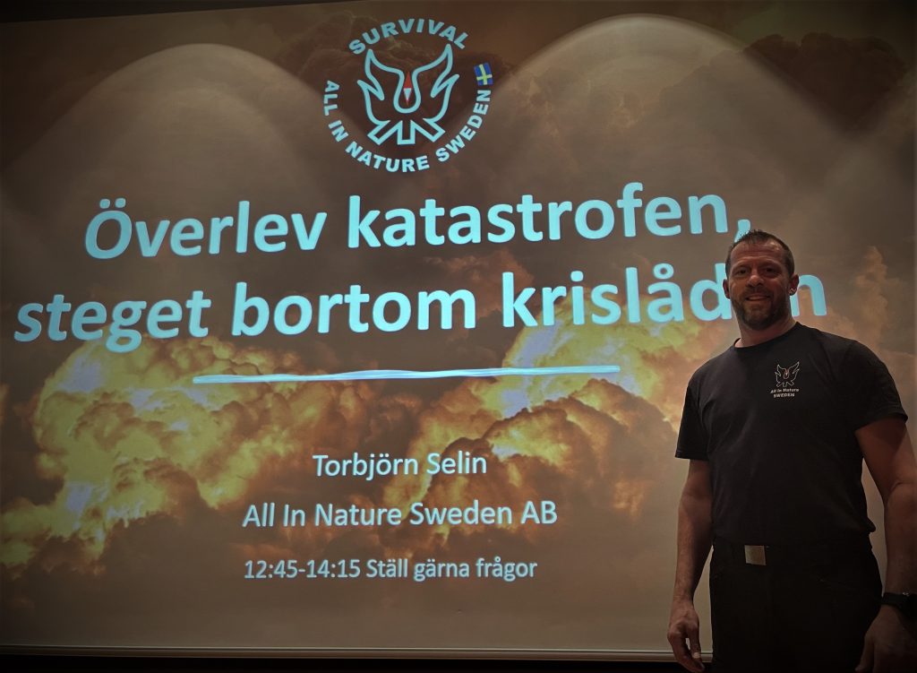 Torbjörn Selin står framför en stor projektorduk som visar startbilden på föreläsningen "Överlev katastrofen - steget bortom krislådan!