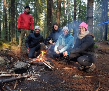 Skogen och elden skapar snabbt gemenskap Killar och tjejer sitter vid elden som de själva skapat