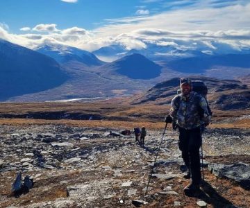 Torbjörn Selin tittar in i kameran i bakgrunden går en grupp fjällvandrare med en vacker dalgång från kungsleden i bakgrunden