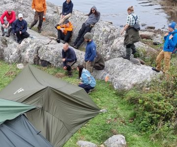 En grupp kursdeltagare vid kustöverlevnad samlas kring ett skydd av presennig vid havet