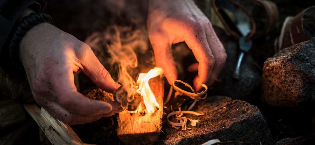 Två händer vid en liten eld av näver första steget vid tändning