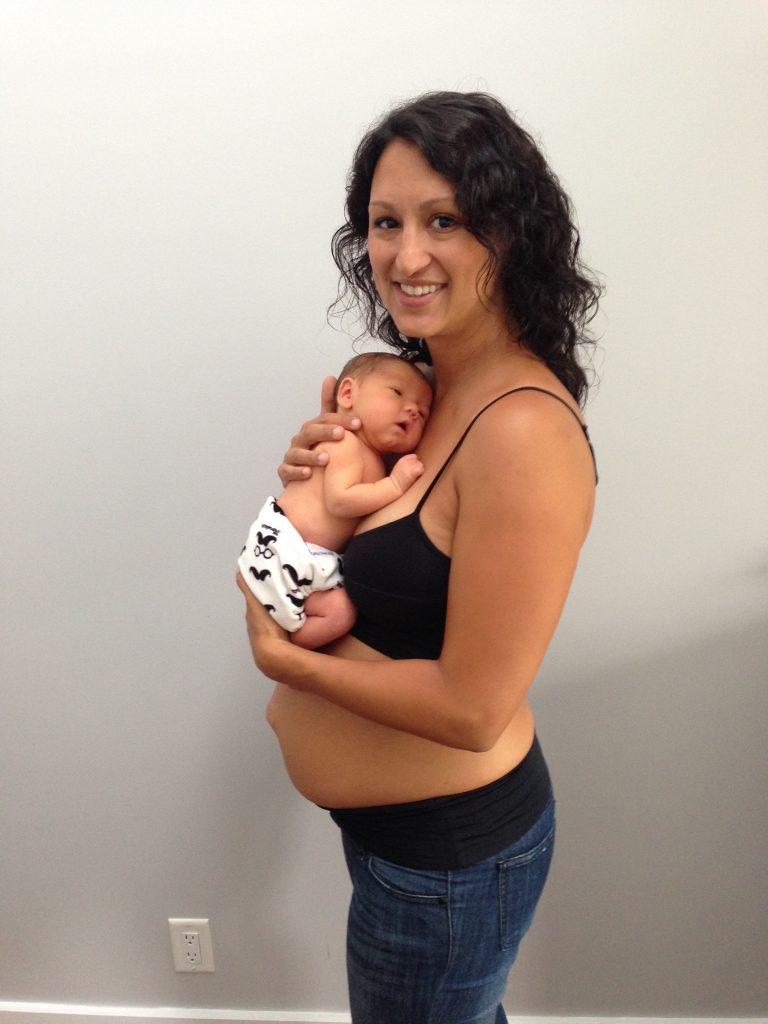 A new mother holds her newborn baby. She has a visible diastasis recti . (abdominal separation)