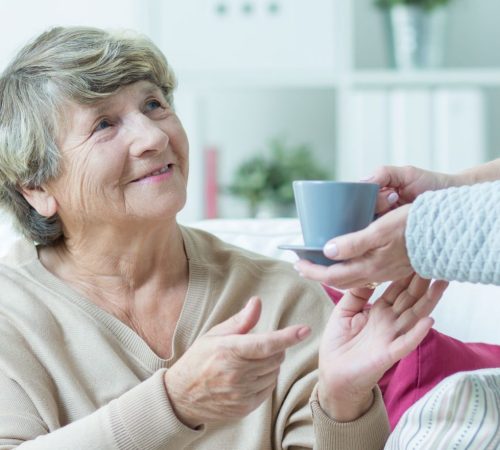 Carer is giving cup of tea to elderly woman