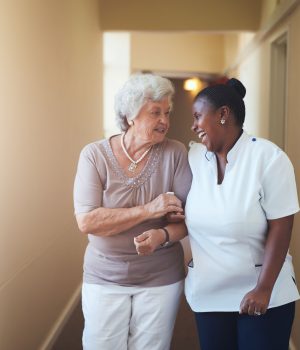 Portrait of happy female caregiver and senior woman walking together at home. Professional caregiver taking care of elderly woman.