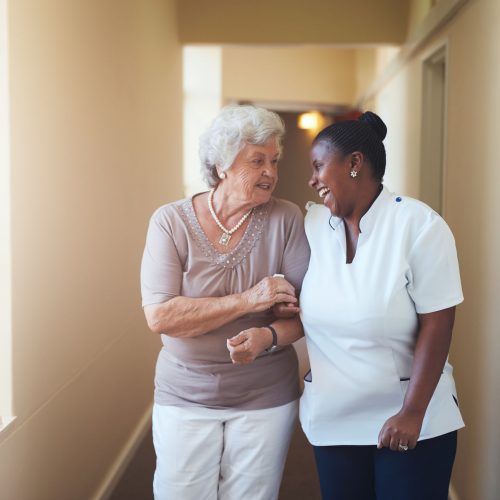 Portrait of happy female caregiver and senior woman walking together at home. Professional caregiver taking care of elderly woman.