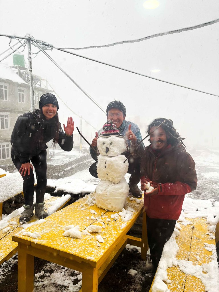 Laurence, Joshua, and the owner of the bakery building a snowman at the bakery in Langtang