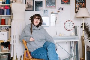 Amber Hards sitting in front of a knitting machine in her studio