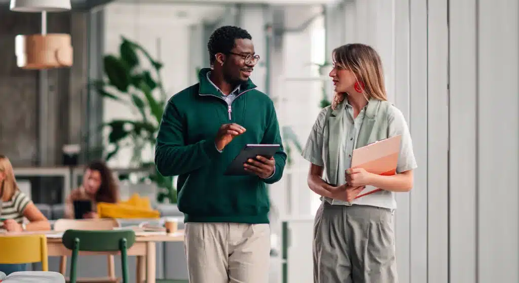 Two young professionals discussing while walking in the office