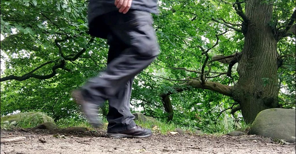 person on path in wood in mid step, right leg blurred