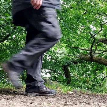 person on path in wood in mid step, right leg blurred