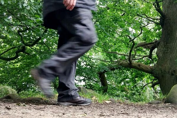 person on path in wood in mid step, right leg blurred