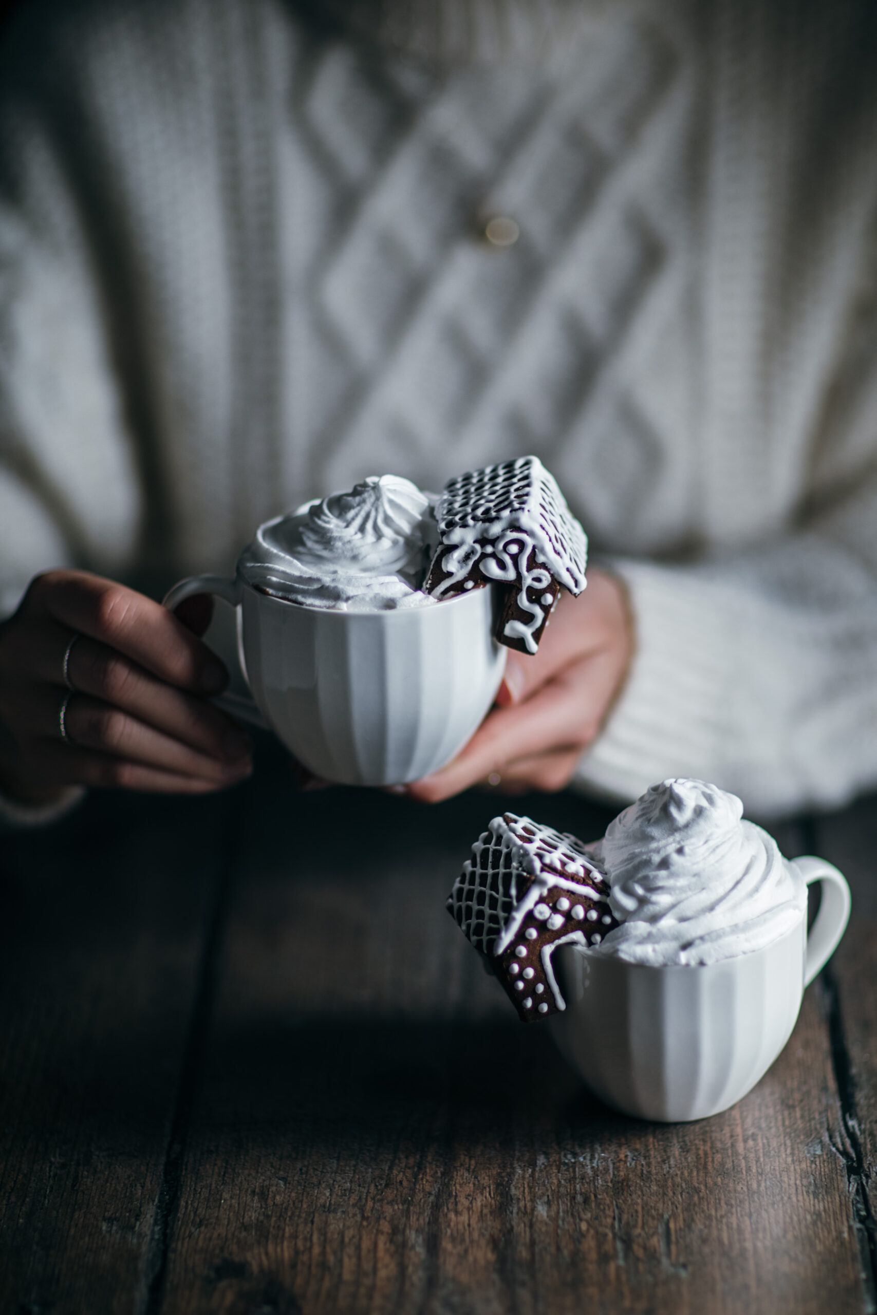 Two glasses of hot chocolate with cream and small gingerbread houses