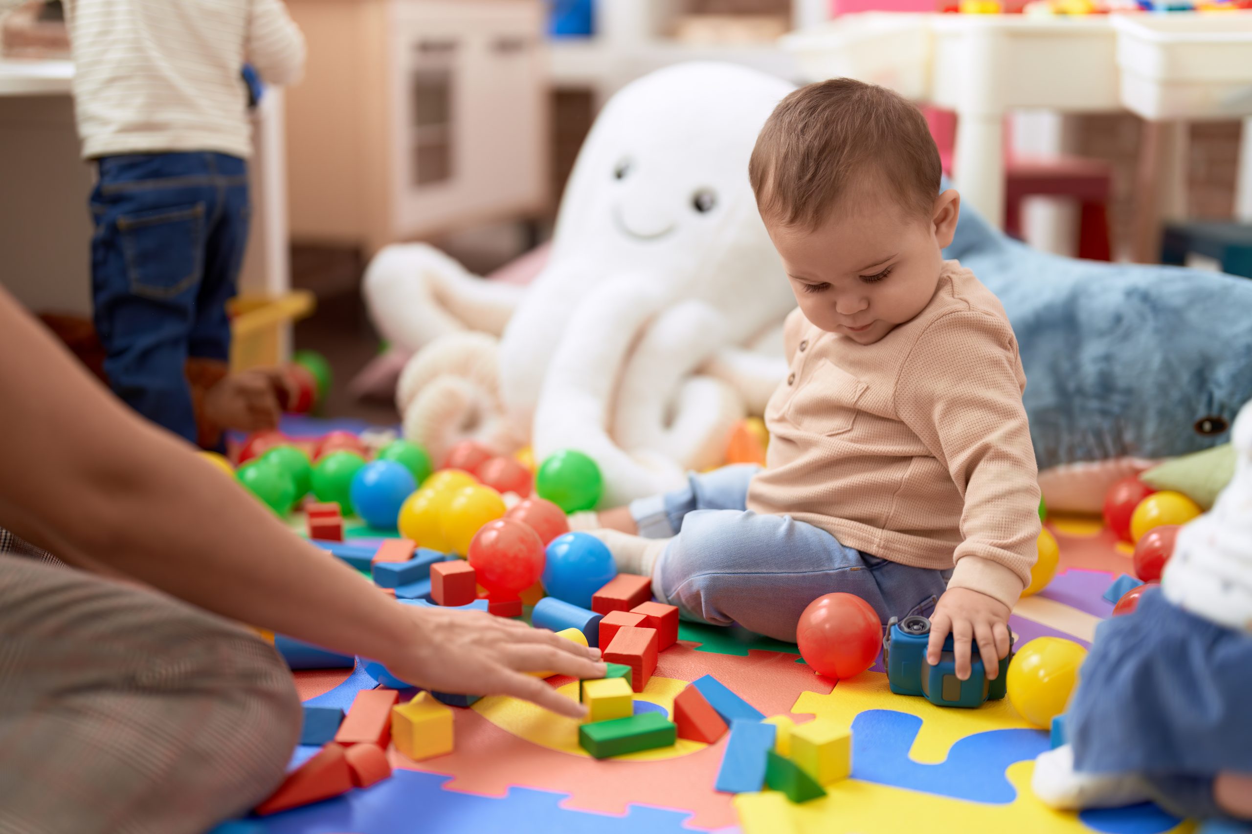 Adorable toddler playing with toys sitting on floor at kindergarten