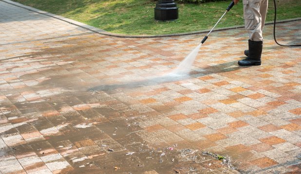 A man uses a pressure washer to clean a brick walkway, removing dirt and grime from the surface.