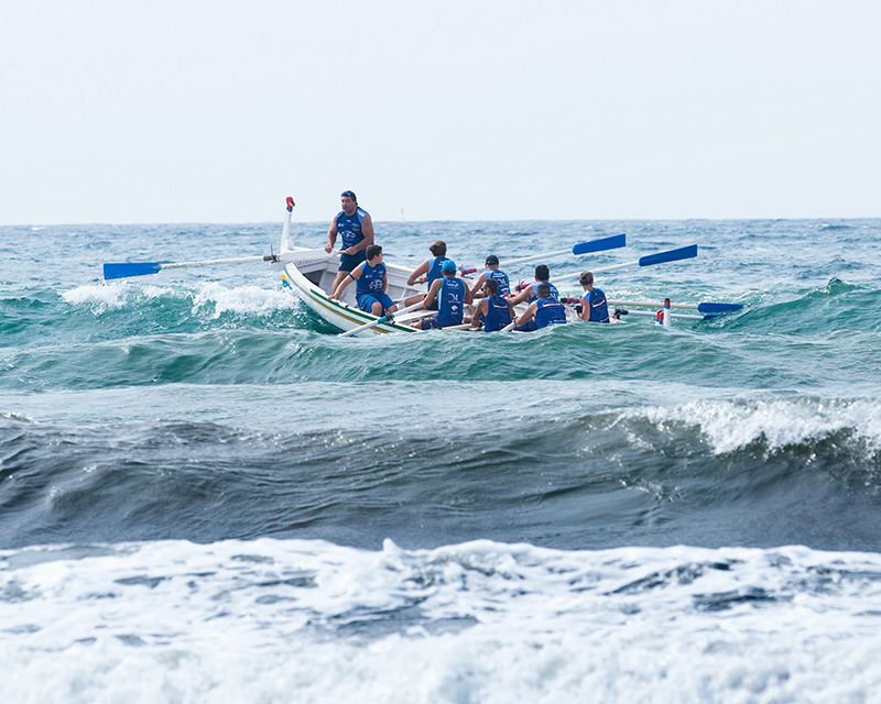 Een groep mensen zit in een roeibootje op zee en bedwingt als een hecht team de golven