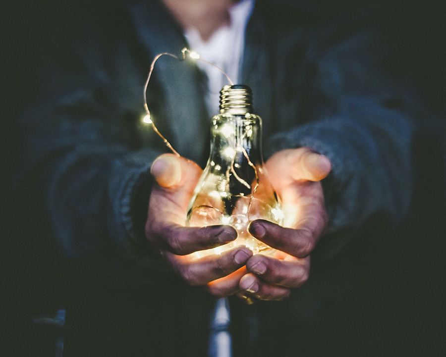 Een man heeft een gloeilamp met kleine brandende lichtjes in zijn twee uitgstoken handen