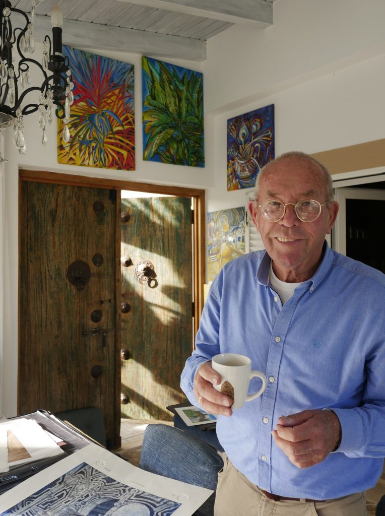 The Artist Michael J Webster with paintings in the background. Photocredit: Catrin Ponciano