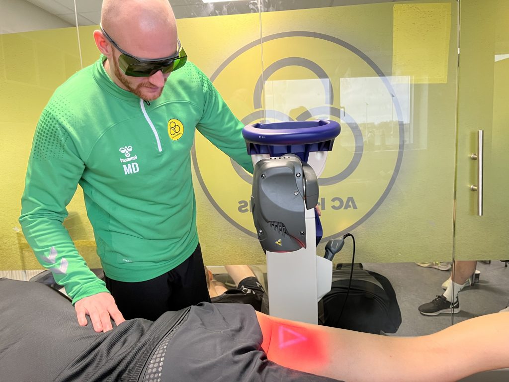 Fysioterapeut behandler fodboldspiller med laserterapi mod sportsskader.