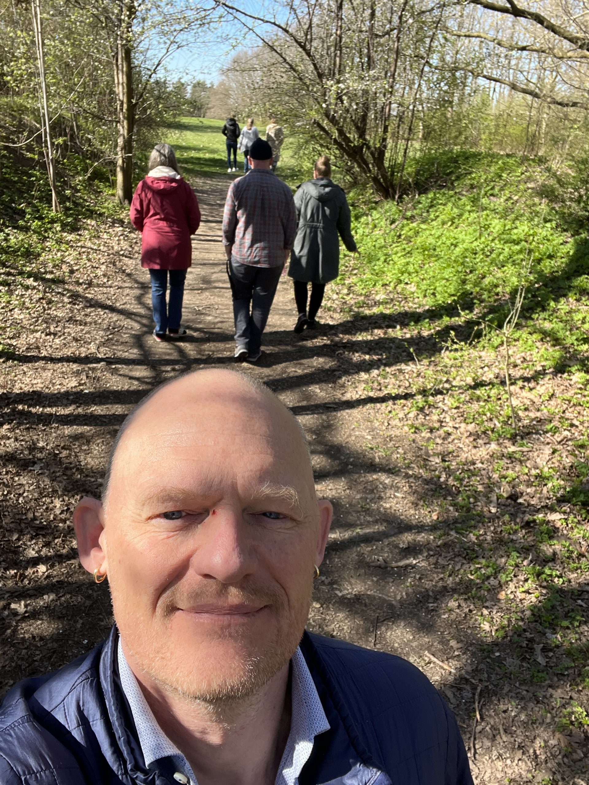 Foto af Asger Johannes Steenholdt med flere vandrende perosner i baggrunden udenfor på en skovsti