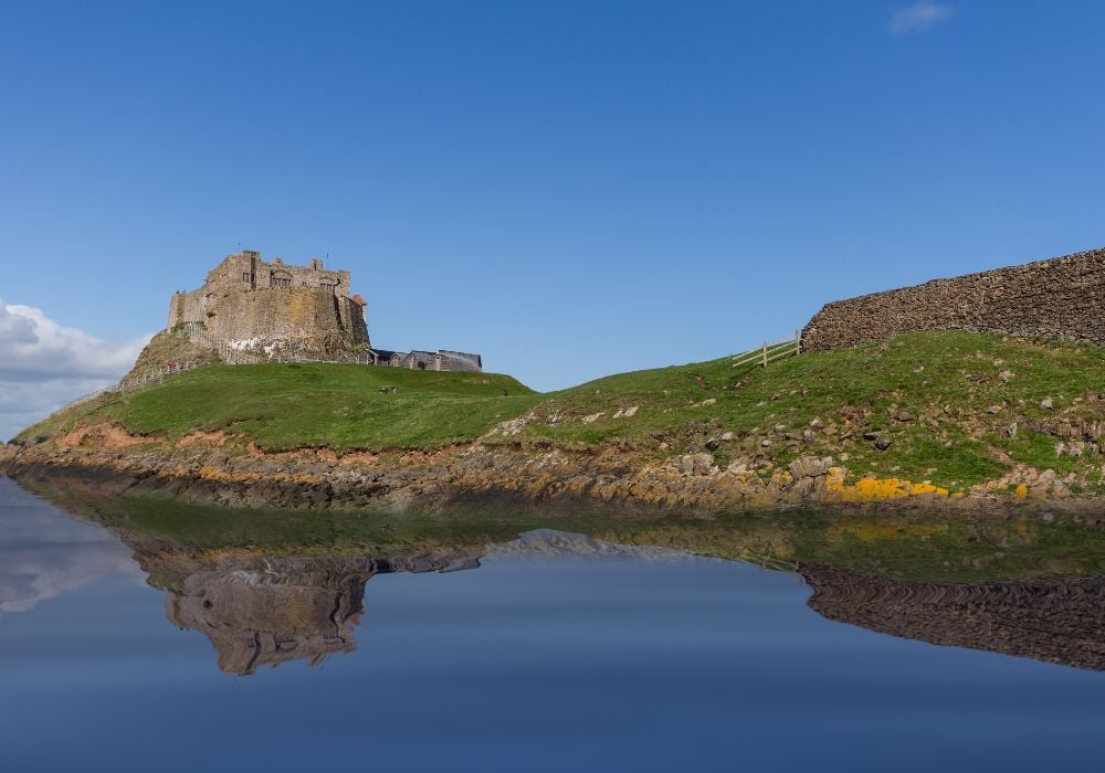 A stunning view of Lindisfarne Castle in England with clouds and blue sky behind it
