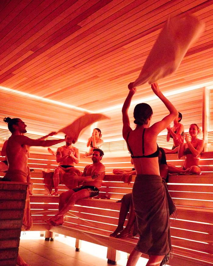 People sitting in the sauna at Othership; two people are waving towels over them