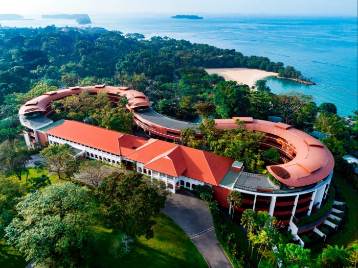 An aerial shot of Capella resort, which sits on top of a hill on Sentosa Island, surrounded by greenery and overlooking the sea