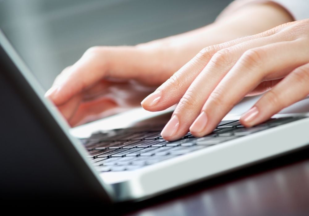 Image of human hands pressing laptop keys for computer work.