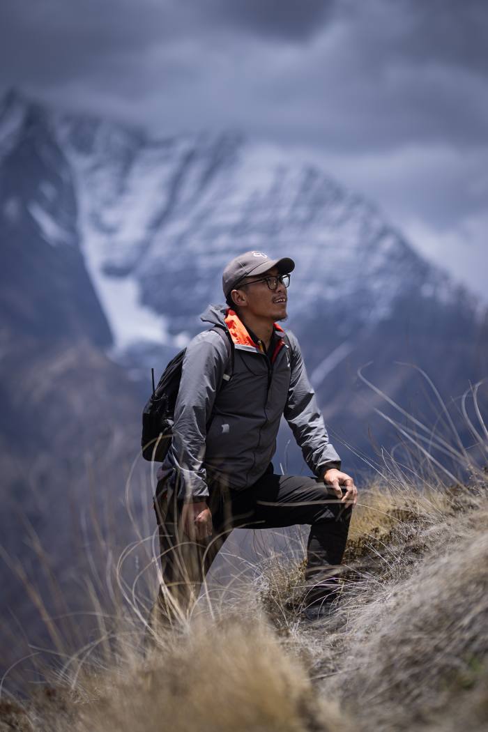 A man in hiking gear and cap stands in a mountainous landscape