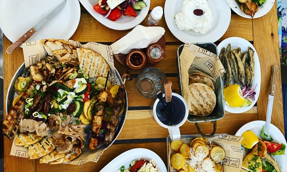 table filled with greek food tzatziki, bread, meat, olive oil, salad in mykonos greece