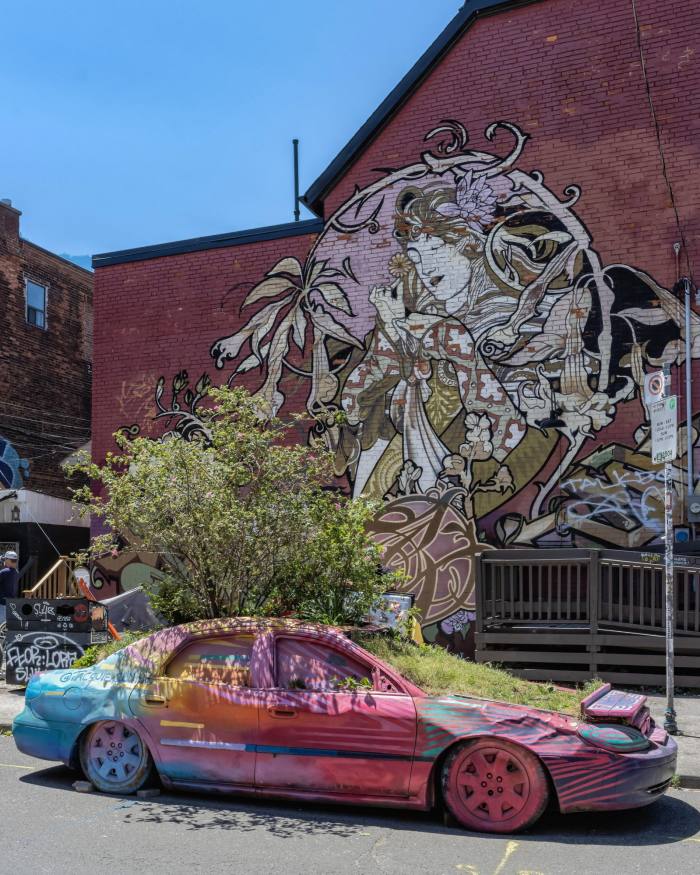 The Garden Car in Kensington Market – an old sedan spray-painted in many bright colours and with greenery growing from its roof and bonnet
