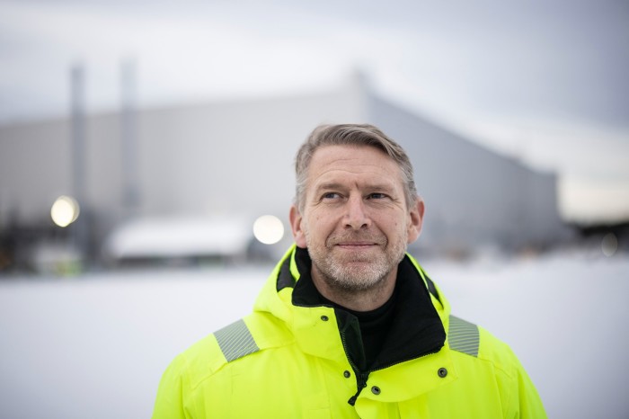 Peter Carlsson, wearing a high vis coat with an out-of-focus factory behind him