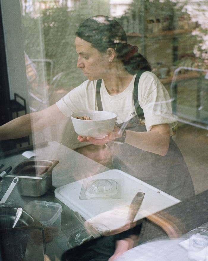 A female employee of the café holding a bowl of cereal in a kitchen space