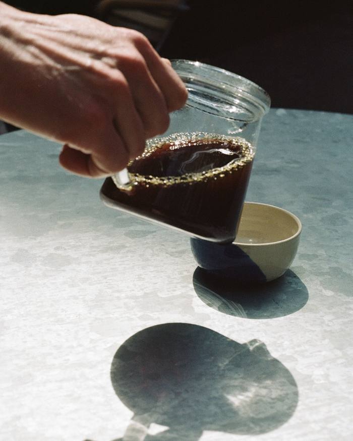  A hand pouring coffee into a cup from a glass vessel