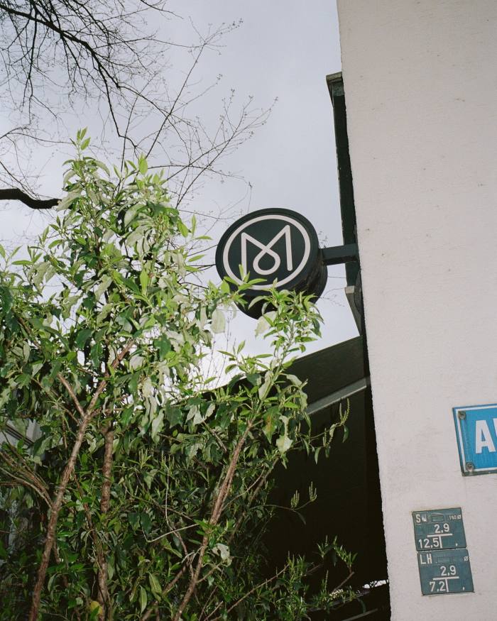 Monocle’s M logo on a round sign sticking out from the facade of the brand’s Zürich headquarters 