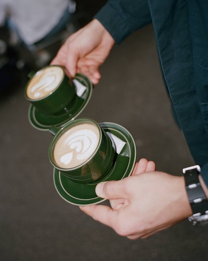 A man holding two cups of coffee at Monocle Café