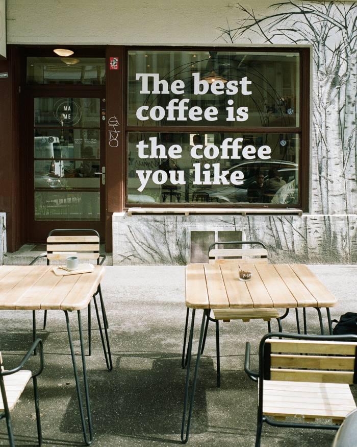 Wooden seating and chairs outside Mame, on the main window of which is inscribed: ‘The best coffee is the coffee you like’
