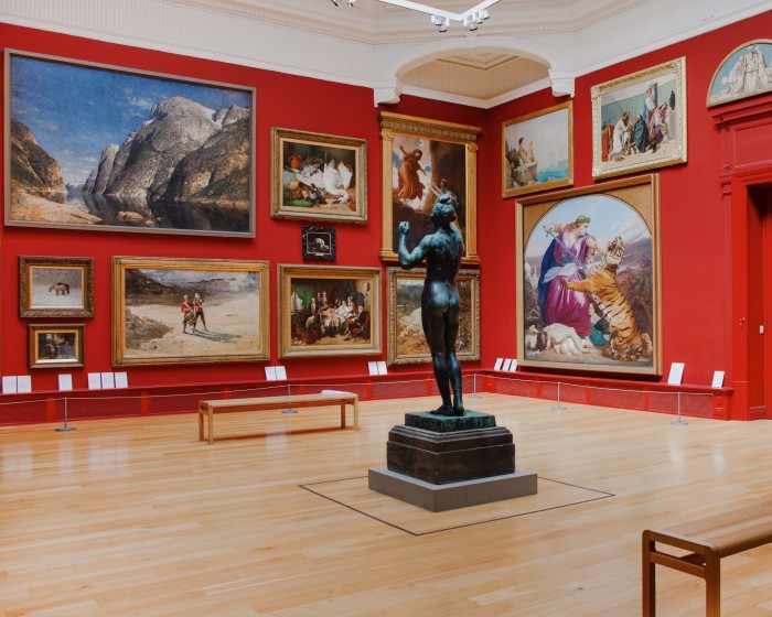 A red art gallery wall covered in paintings, with a statue in the middle of the room