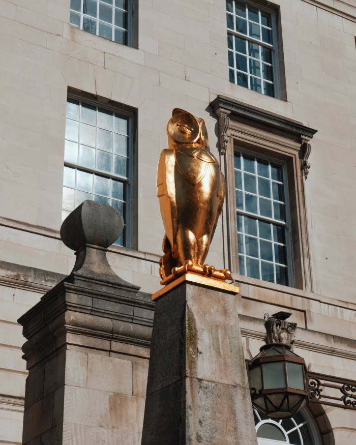 A gilded sculpture of an owl in front of a building of grey stone