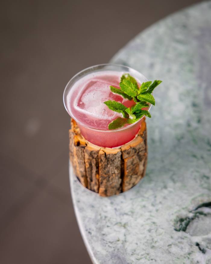 Popinjays’ Cotton Tree cocktail – a dark-pink drink in a small triangular glass held within a rough-hewn wood container