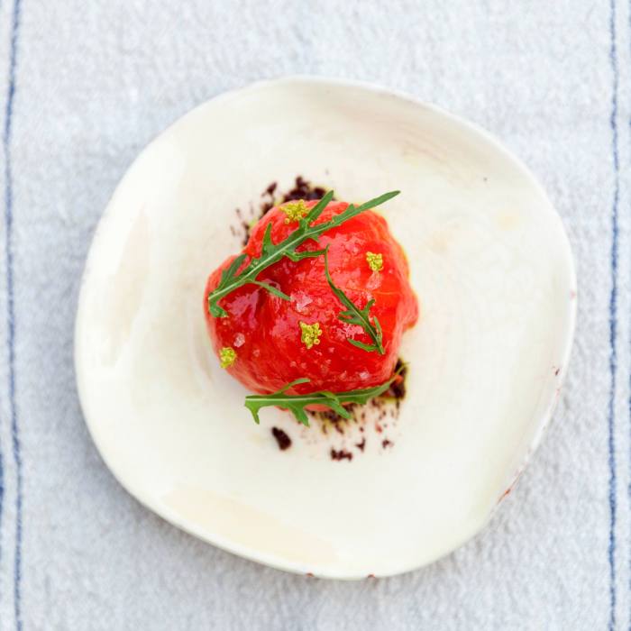 A tomato, decorated with rocket leaves and flowers, on a white plate