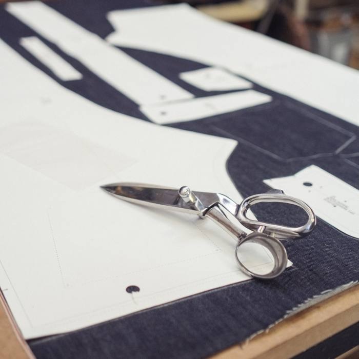A denim textile is laid out on a table with scissors and a paper pattern