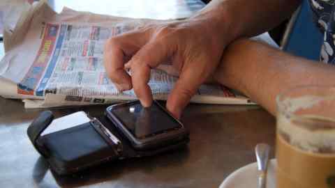 Picture of a person’s hand tapping away at a gambling app on their mobile phone while their arm rests on a newpaper open at gambling adverts