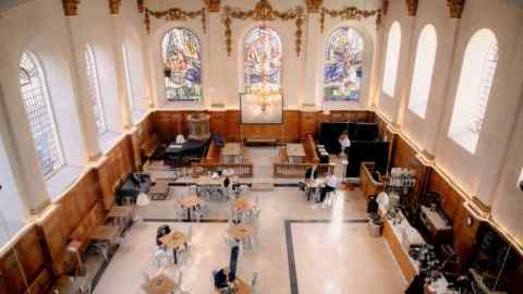 The Wren Coffee at St Nicholas Cole Abbey, with large arched and stained-glass windows surrounding a space dotted with tables and chairs