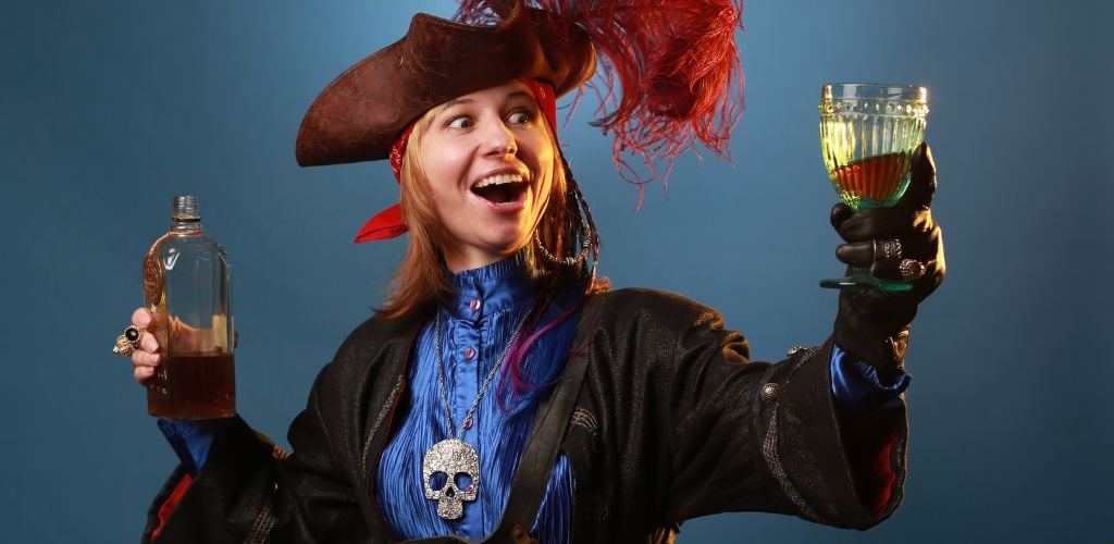 A woman dressed as a pirate holds a bottle of rum and a glass of rum. 