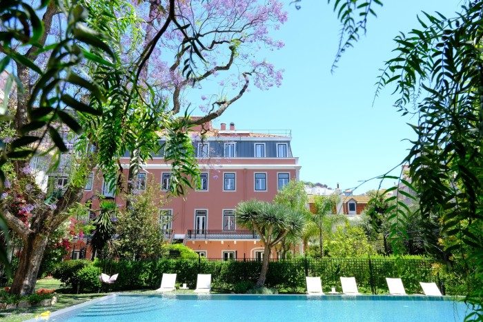 The foliage-surrounded pool at Lisbon’s 19th-century Palácio Príncipe Real, with the pink facade of the hotel itself behind it