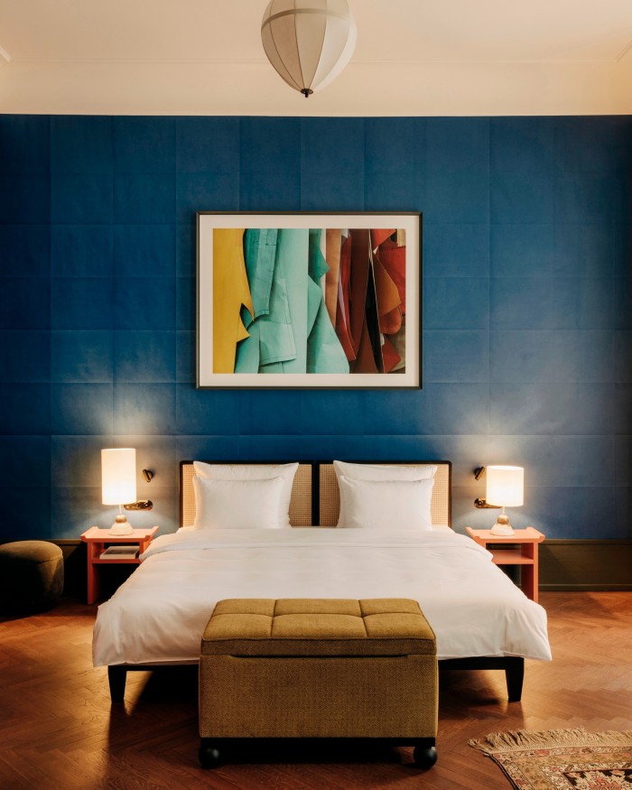 A room in Berlin’s Château Royal; behind the bed is a blue wall on which hangs an abstract artwork